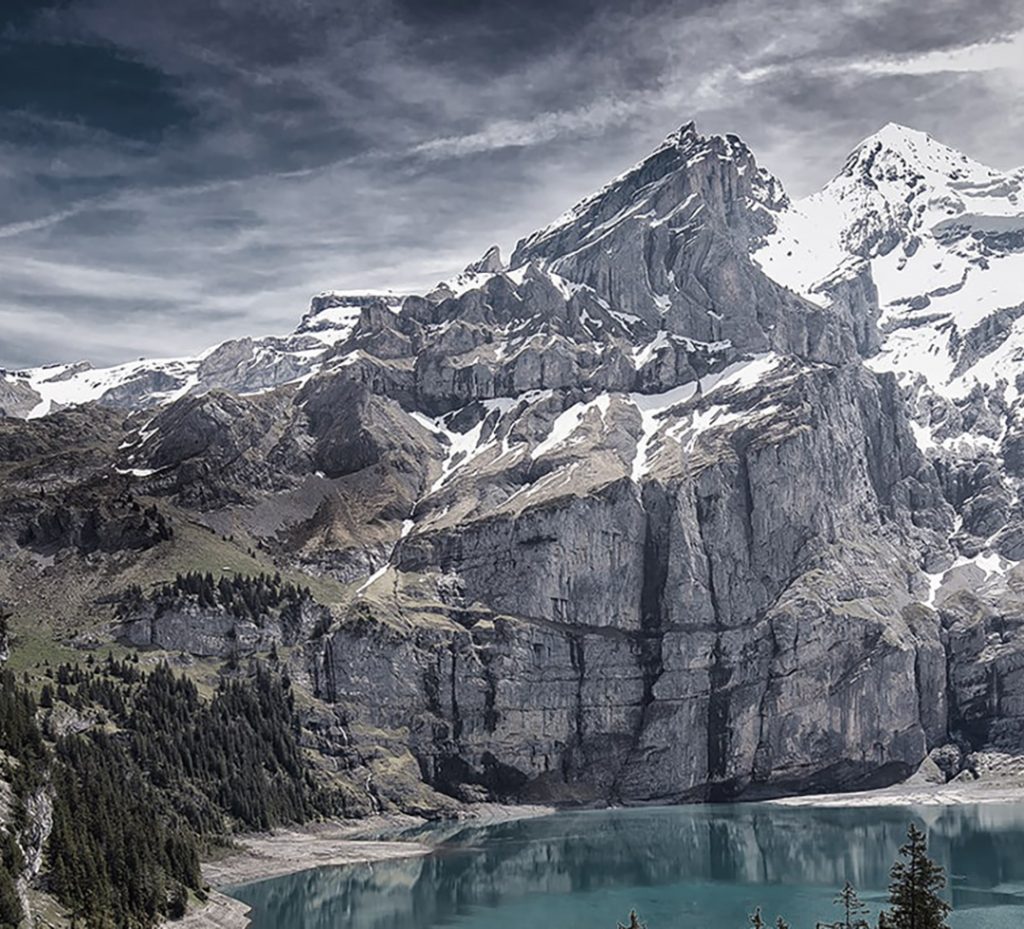 Un lac dans une vallée alpine encaissée entouré de sapins et de monts enneigés.